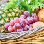 Keranjang hampers buah segar berisi anggur, nanas, dan delima